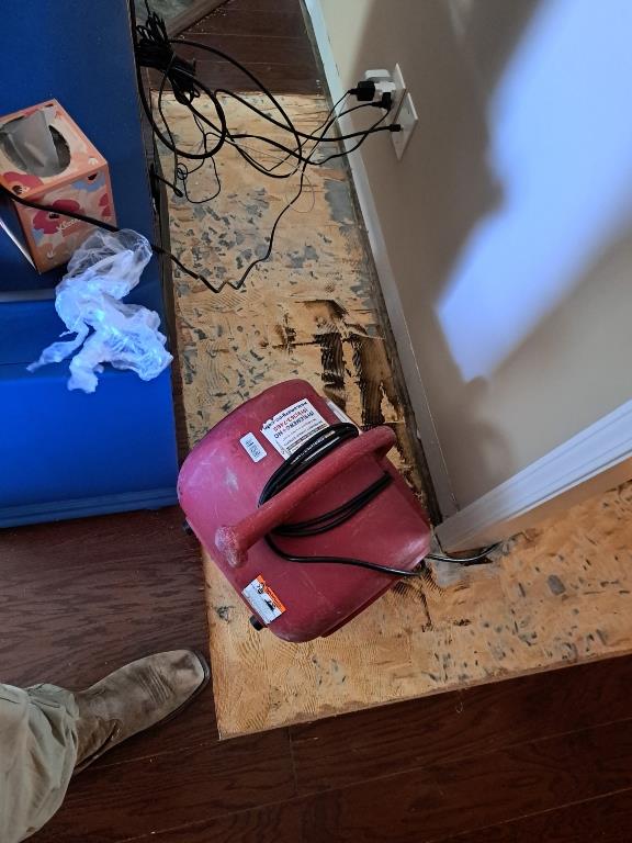 Water-damaged hardwood flooring with visible warping. Drying equipment in place.