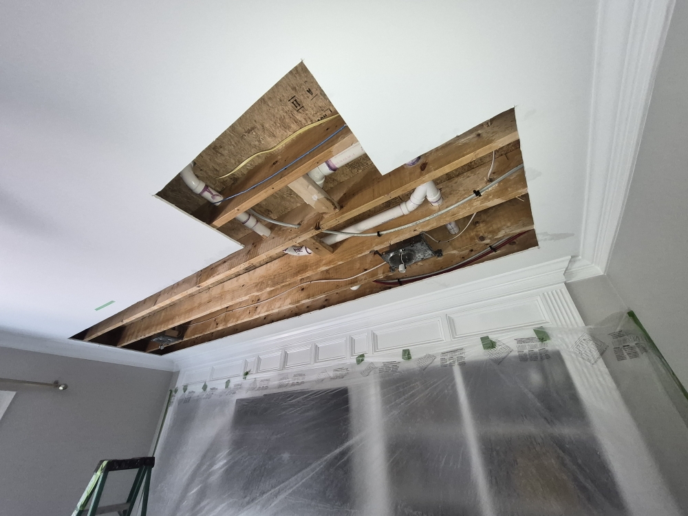 Cleanly cut ceiling opening exposing wet structural cavity for professional drying after a toilet overflow water damage loss in Fuquay Varina NC