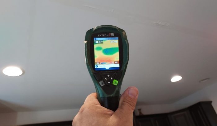 Hand holding a thermal imaging camera detecting hidden water damage in a home.